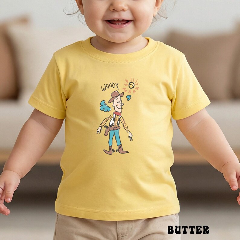 May include: A yellow t-shirt featuring a cartoon illustration of Woody from Toy Story. The design includes the word "WOODY" above the character, with a sun and cloud graphic. The shirt is made of a soft material and is suitable for children.