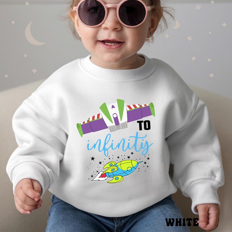 May include: White sweatshirt with a colorful graphic featuring a rocket ship and the phrase "TO infinity" in blue. The design includes green, purple, and red accents. The word "WHITE" is printed at the bottom.