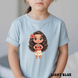 May include: Light blue t-shirt featuring a cartoon illustration of a character with long, wavy brown hair, a red flower, and a red and white outfit. The text "LIGHT BLUE" is printed at the bottom of the shirt.