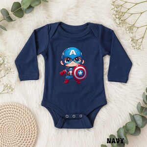 Op de afbeelding: Marineblauwe babybody met lange mouwen. De body heeft een cartoonillustratie van Captain America met een schild. Het ontwerp bevat de letter "A" op de helm van het personage. Het woord "NAVY" staat onderaan gedrukt.