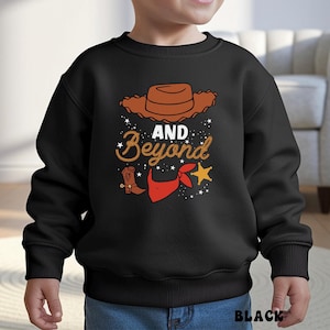 May include: Black sweatshirt with a cowboy-themed graphic. The design includes a brown cowboy hat, a cowboy boot, a red bandana, and a gold star. The words "AND Beyond" are written in a decorative font. The word "BLACK" is printed at the bottom.