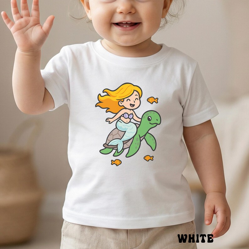 Puede incluir: Camiseta blanca con una sirena de dibujos animados montada en una tortuga marina verde, rodeada de peces naranjas. La sirena tiene pelo rubio y una cola azul. La palabra "WHITE" est&aacute; impresa en la parte inferior.