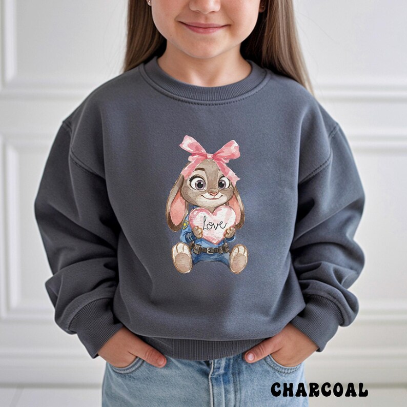 Peut inclure: Sweat-shirt gris anthracite avec une illustration &agrave; l'aquarelle d'un lapin tenant un c&oelig;ur avec le mot "love". Le lapin porte un n&oelig;ud rose et une salopette bleue. Le mot "CHARCOAL" est imprim&eacute; en bas de l'image.