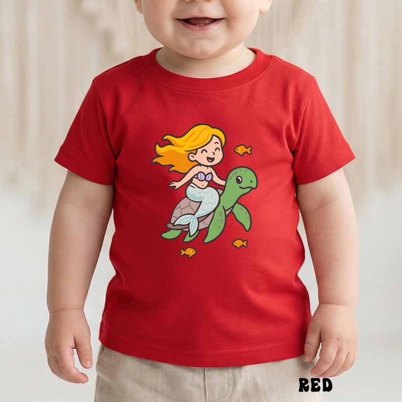 Puede incluir: Camiseta roja para ni&ntilde;os peque&ntilde;os con una sirena de dibujos animados montada en una tortuga verde, rodeada de peque&ntilde;os peces amarillos. La sirena tiene el pelo rubio y una cola azul. La palabra "RED" est&aacute; impresa en la parte inferior.