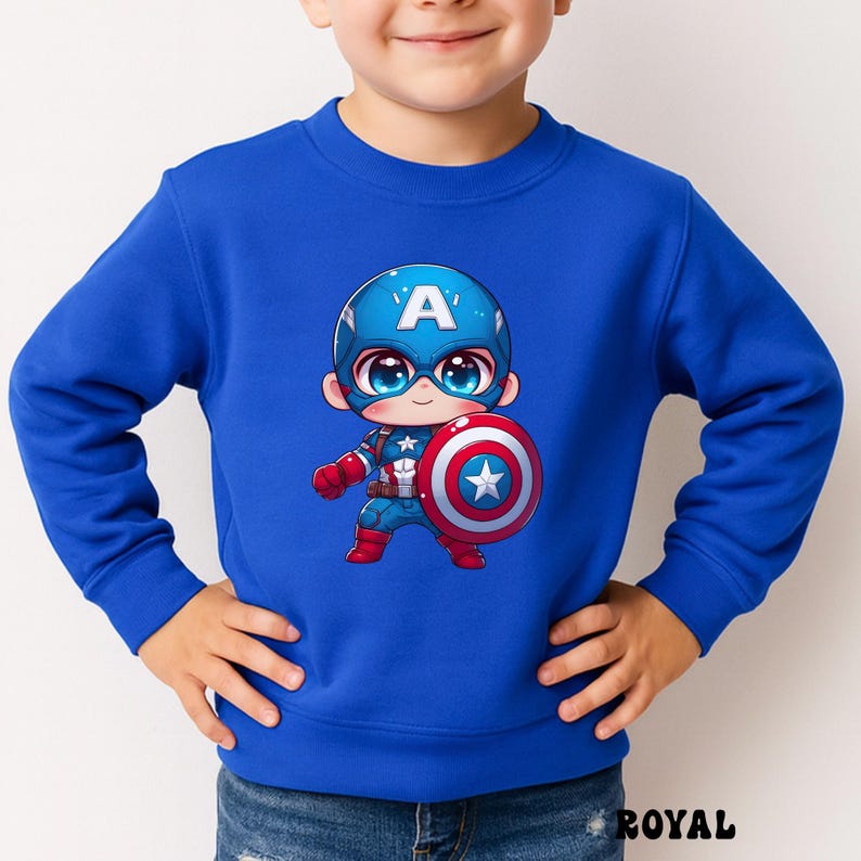 Op de afbeelding: Koningsblauw sweatshirt met een cartoon Captain America-afbeelding. De afbeelding toont Captain America met een blauwe helm met een witte "A", die een schild met een ster vasthoudt. De sweatshirt heeft een ronde hals.