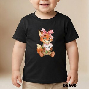 Peut inclure: T-shirt noir avec une illustration &agrave; l'aquarelle d'un renard avec un n&oelig;ud rose, tenant un c&oelig;ur avec le mot "love". Le renard est orange et blanc, avec des accents verts. Le mot "BLACK" est imprim&eacute; en bas du t-shirt.