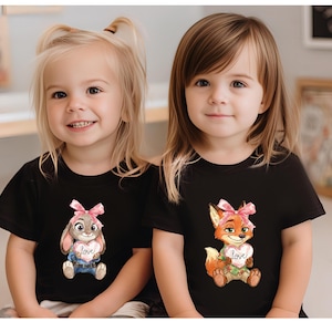 Peut inclure: Deux jeunes filles portant des t-shirts noirs. L'un pr&eacute;sente un lapin tenant un c&oelig;ur avec "love", l'autre un renard avec un c&oelig;ur. Les deux personnages ont des n&oelig;uds roses. Les filles sourient.