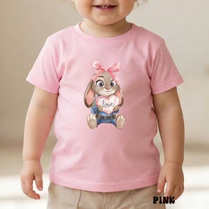 Peut inclure: T-shirt rose &agrave; manches courtes avec un lapin de dessin anim&eacute; tenant un c&oelig;ur avec le mot "Love". Le lapin porte un n&oelig;ud rose et une veste et un jean bleus. Le t-shirt est en mati&egrave;re souple.