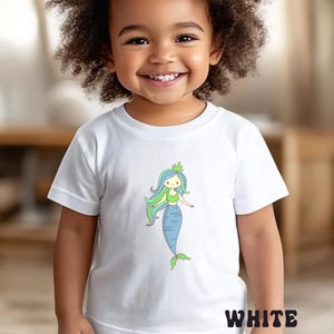 Puede incluir: Camiseta blanca con una ilustraci&oacute;n de sirena de dibujos animados. La sirena tiene pelo azul y verde, un top verde y una cola azul. La palabra "WHITE" est&aacute; impresa en blanco en la parte inferior de la camiseta.