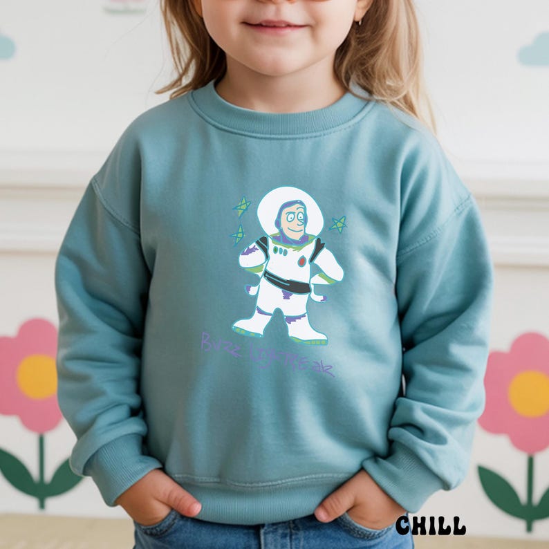 May include: A teal sweatshirt featuring a graphic of Buzz Lightyear in a white spacesuit with green accents. The text "Buzz Lightyear" is printed in a light purple script below the character. The word "CHILL" is printed in black at the bottom.