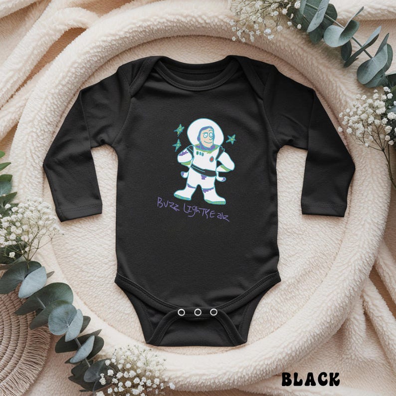 May include: Black baby bodysuit with long sleeves. The bodysuit features a cartoon graphic of Buzz Lightyear in a white spacesuit with green and purple accents. The text "Buzz Lightyear" is written in purple script below the graphic. The word "BLACK" is at the bottom.