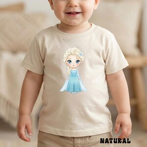 Puede incluir: Camiseta beige con una ilustraci&oacute;n de dibujos animados de una princesa con un vestido azul, trenza rubia y flor azul. La palabra "NATURAL" est&aacute; impresa en negro en la parte inferior de la camiseta.