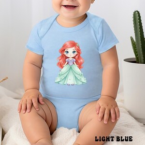 Puede incluir: Un body para beb&eacute; de color azul claro con mangas cortas y una ilustraci&oacute;n central de un personaje de dibujos animados con largo cabello rojo, que viste un corpi&ntilde;o morado y un vestido verde menta con peque&ntilde;os lazos.
