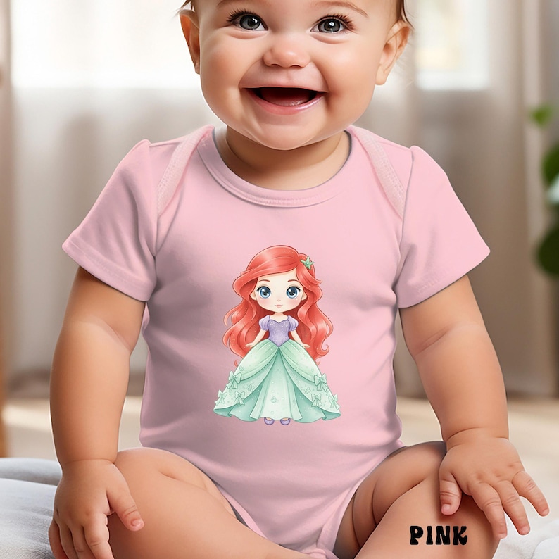 Puede incluir: Un body de beb&eacute; de color rosa claro de manga corta con una ilustraci&oacute;n gr&aacute;fica central de un personaje de dibujos animados con largo cabello rojo, que viste un corpi&ntilde;o morado y un vestido verde claro con peque&ntilde;os lazos. La palabra PINK est&aacute; en negro.