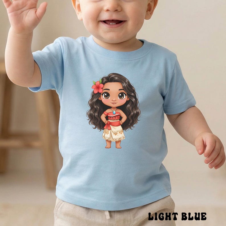 May include: Light blue toddler t-shirt featuring a cartoon illustration of a girl with long, dark wavy hair, a red flower, and a red and white outfit. The text "LIGHT BLUE" is printed at the bottom.