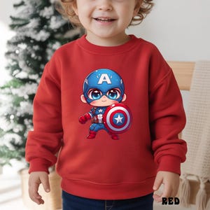 Op de afbeelding: Een rode sweatshirt met een cartoon illustratie van Captain America. Het personage draagt een blauwe helm met een witte "A", een blauw en rood pak en een schild. Het woord "RED" staat onderaan.