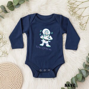 May include: Navy blue baby bodysuit with long sleeves. The front features a cartoon illustration of Buzz Lightyear in a white spacesuit with green and purple accents. The text "Buzz Lightyear" is written below the character in a playful font.