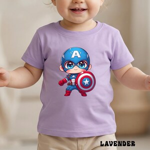 Op de afbeelding: Een lavendelkleurig T-shirt met een cartoonafbeelding van Captain America. De illustratie toont Captain America met een blauwe helm, schild en kostuum. Het woord "LAVENDER" staat onderaan de afbeelding.