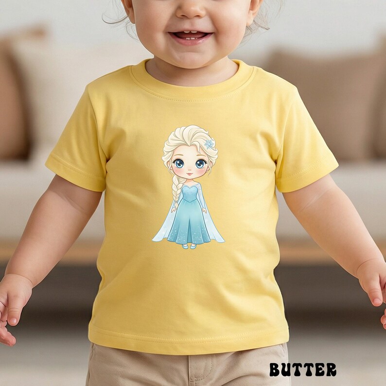 Puede incluir: Una camiseta amarilla de manga corta con una ilustraci&oacute;n de dibujos animados de una princesa con un vestido azul. La princesa tiene el pelo rubio y un accesorio azul para el pelo. La palabra "BUTTER" est&aacute; impresa en negro en la parte inferior de la camiseta.
