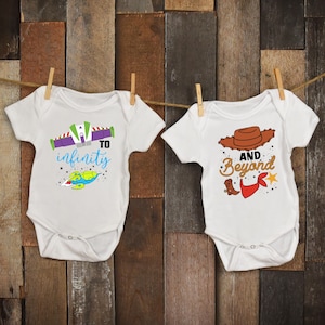 May include: Two white baby onesies with cartoon graphics. One says "To Infinity" with a spaceship design. The other says "And Beyond" with a cowboy hat and boot design. Both are hanging on a wooden background.