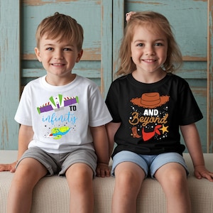 May include: Two children wearing matching t-shirts. One shirt is white with a rocket ship graphic and the words "To Infinity" in blue and purple. The other shirt is black with a cowboy hat and the words "And Beyond".