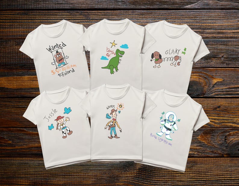 May include: Six white t-shirts with cartoon character designs. One shirt has "Wanted" and "$50 Billion Reward" text. Other shirts feature a dinosaur, a dog, a cowgirl named Jessie, Woody, and Buzz Lightyear. The shirts are on a wooden background.