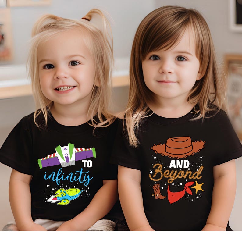 May include: Two young children wearing black t-shirts. One shirt says "To infinity" with a spaceship graphic. The other shirt says "And Beyond" with a cowboy hat, boot, and bandana graphic. Both shirts have colorful designs.