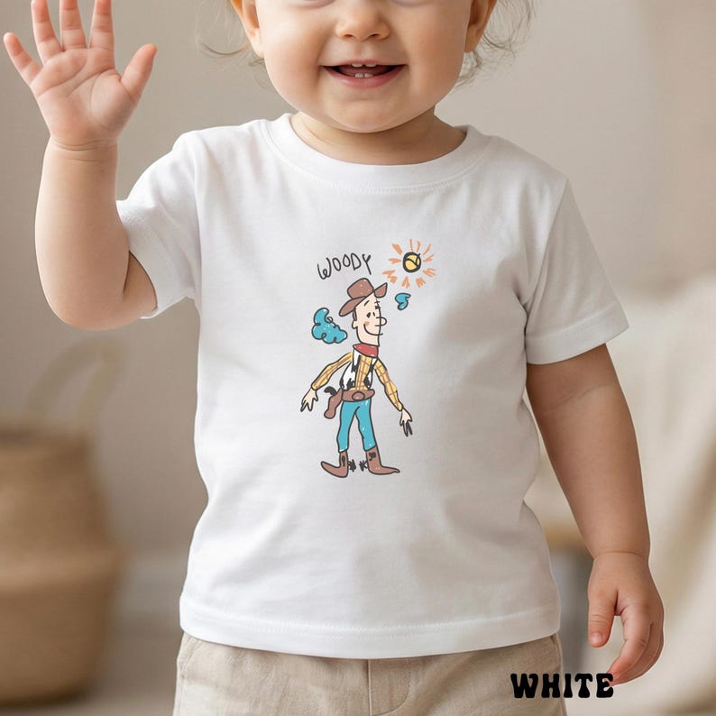 May include: White t-shirt featuring a cartoon illustration of Woody from Toy Story. The design includes Woody in a cowboy hat, a yellow plaid shirt, blue pants, and brown boots. The word "WOODY" is written above the character.