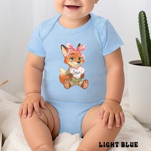 Peut inclure: Body b&eacute;b&eacute; bleu clair avec un renard de dessin anim&eacute; tenant un c&oelig;ur avec le mot "Love". Le renard a une fourrure orange, un n&oelig;ud rose et porte une chemise hawa&iuml;enne. Le texte "LIGHT BLUE" est en bas.