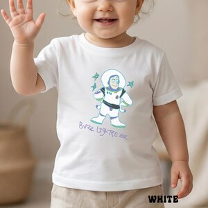 May include: White t-shirt featuring a cartoon illustration of Buzz Lightyear with the text "Buzz Lightyear". The shirt has a crew neck and short sleeves. The word "WHITE" is printed at the bottom of the shirt.