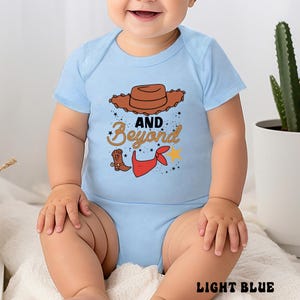 May include: Light blue baby bodysuit with a cowboy theme. The design includes a brown cowboy hat, a cowboy boot, a red bandana, and the words "AND Beyond" in a playful font. The text "LIGHT BLUE" is at the bottom.