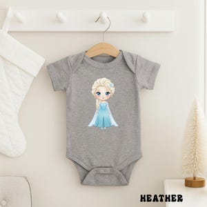 Puede incluir: Un body de beb&eacute; gris con una ilustraci&oacute;n de dibujos animados de una princesa con un vestido azul. La princesa tiene el pelo rubio y ojos azules. La palabra "HEATHER" est&aacute; impresa en negro en la parte inferior de la imagen.