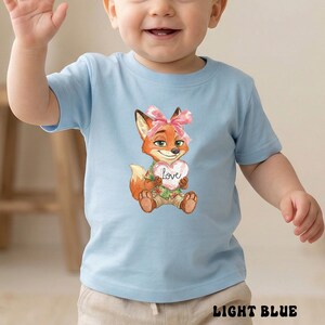 Peut inclure: T-shirt bleu clair pour enfant avec un renard de dessin anim&eacute; tenant un c&oelig;ur avec le mot "Love". Le renard porte un n&oelig;ud rose et une chemise hawa&iuml;enne. Le texte "LIGHT BLUE" est en bas.