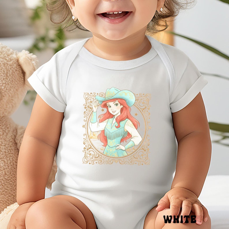 K&ouml;nnte beinhalten: Wei&szlig;er Baby-Body mit einer Cartoon-Illustration einer Cowgirl mit roten Haaren und blauem Hut. Das Design ist von einem goldenen Zierrahmen umgeben. Das Wort "WHITE" ist unten aufgedruckt.
