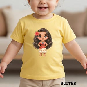 May include: A yellow t-shirt featuring a cartoon illustration of a character with long dark hair, a red flower, and a red and white outfit. The word "BUTTER" is printed in black at the bottom of the shirt.