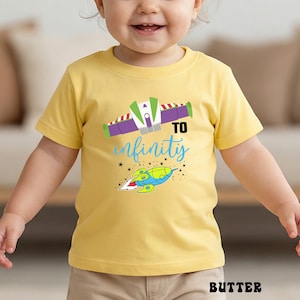 May include: A yellow t-shirt with a colorful graphic featuring a spaceship and the words "To infinity" in blue script. The design includes a spaceship and stars. The word "BUTTER" is printed at the bottom.