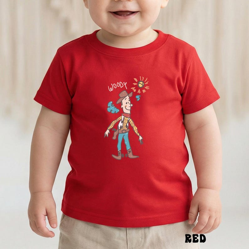 May include: A red short-sleeve t-shirt featuring a cartoon illustration of Woody from Toy Story. The illustration includes Woody's hat, vest, and a sun graphic. The word "WOODY" is written above the character. The word "RED" is written at the bottom of the shirt.