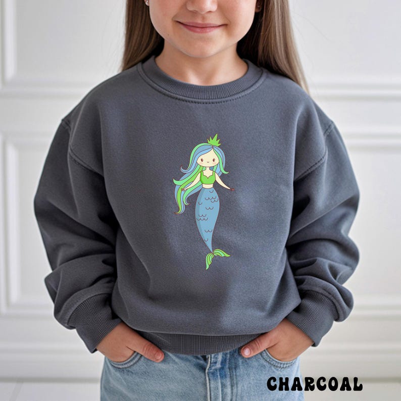 Puede incluir: Sudadera gris carb&oacute;n con una sirena de dibujos animados con pelo azul y verde, un top verde y una cola azul. La palabra "CHARCOAL" est&aacute; impresa en la parte inferior. La sudadera la lleva una persona.