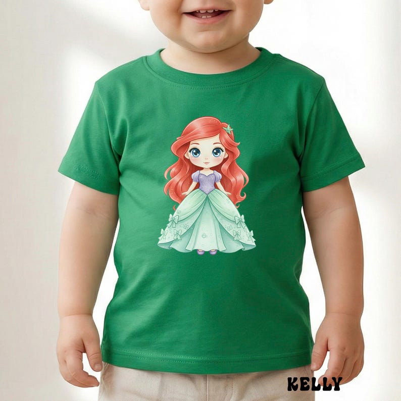 Puede incluir: Una camiseta verde de manga corta con un gr&aacute;fico central de un personaje de dibujos animados con largo cabello rojo, que viste un corpi&ntilde;o morado y un vestido de gala verde claro con peque&ntilde;os lazos. El nombre KELLY est&aacute; impreso en negro abajo.