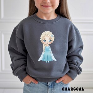 Puede incluir: Sudadera gris carb&oacute;n con una ilustraci&oacute;n de dibujos animados de una princesa con un vestido azul y una trenza larga. La princesa tiene el pelo rubio y ojos azules. La palabra "CHARCOAL" est&aacute; impresa en blanco en la parte inferior de la imagen.