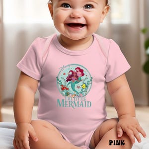 May include: Pink baby bodysuit featuring a circular graphic of Ariel and Flounder from Disney's The Little Mermaid. The design includes the Disney logo and the movie title in teal. The word "PINK" is printed in black at the bottom.
