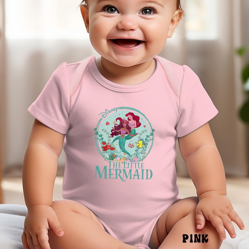 May include: Pink baby bodysuit featuring a circular graphic of Ariel and Flounder from Disney's The Little Mermaid. The design includes the Disney logo and the movie title in teal. The word "PINK" is printed in black at the bottom.