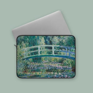 May include: Laptop sleeve featuring a famous impressionist painting of a Japanese footbridge over a pond filled with water lilies. The artwork is predominantly green, blue, and purple, with a white bridge and a black border. The laptop is silver.