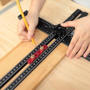 Könnte beinhalten: Ein verstellbarer Winkelmesser für die Holzbearbeitung in Schwarz und Rot mit Zentimetermessungen. Ein gelber Bleistift wird verwendet, um eine Linie auf einem Holzstück zu markieren. Das Lineal hat einen schwarzen Knopf und dient zur präzisen Winkelmessung.