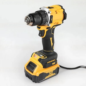 Peut inclure: Une perceuse sans fil jaune et noire. La perceuse a un mandrin argenté et une poignée noire. Le bloc-batterie est jaune et noir avec un logo "XR". Cet outil électrique est conçu pour la construction et les projets de bricolage. Mesures en centimètres.