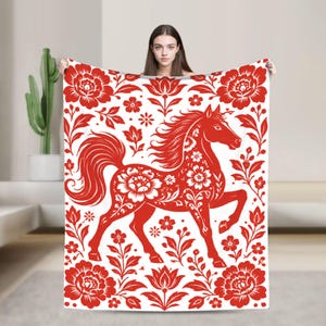 May include: A rectangular throw blanket featuring a vibrant red and white pattern. The design displays a central horse figure adorned with intricate floral motifs, surrounded by a symmetrical arrangement of large blossoms and leafy stems.