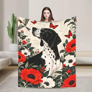 Peut inclure: Un plaid rectangulaire orné d'un chien tacheté noir et blanc entouré de coquelicots rouges éclatants, d'anémones blanches et de plusieurs papillons rouges. Un oiseau est représenté en vol dans le coin supérieur gauche sur fond crème.