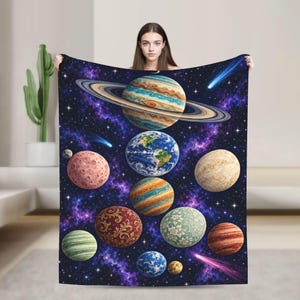 May include: A rectangular throw blanket featuring a deep space galaxy print with purple and blue nebulae. The design displays various planets, including a large ringed planet at the top, Earth, and several textured spheres with floral patterns.