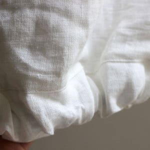 May include: White linen fabric with a gathered edge. The fabric is soft and textured.