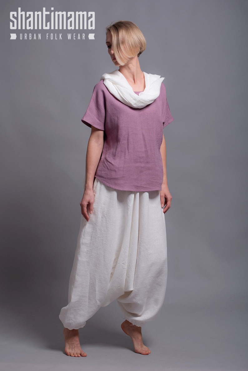May include: A woman wearing a mauve linen top with a white linen scarf and white linen pants. The pants are loose fitting and have a gathered design at the waist.